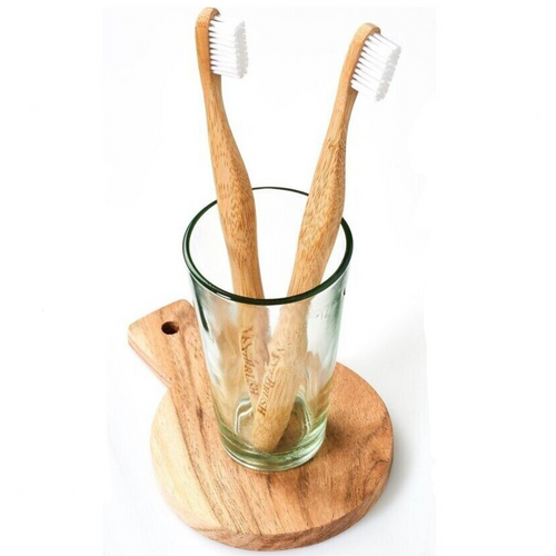 Twee bamboe tandenborstels in een glas op een houten plankje
